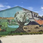 Auf einem Wandbild, dass die gesamte Seite eines großen Hauses einnimmt, ist auf der linken Seite eine intakte, grüne Natur mit einem simbabwischen Kind und Elefanten zu sehen. In der Mitte ist ein Baum, der in seiner Krone die Erdkugel zu umfassend scheint. Rechts sind brennende und qualmende Autreiffen, ausgedörrte Erde und Baumstümpfe in einer giftig aussehenden Landschaft zu sehen.