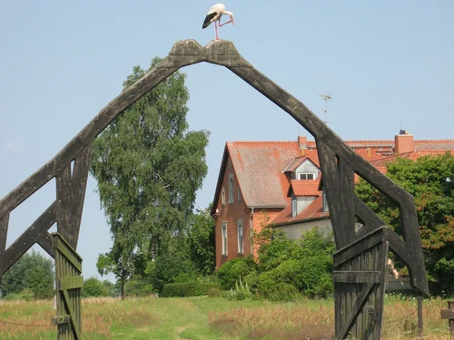Das Portal der Station in Form zweier sich küssender Kraniche mit einem echten Storch darauf sitzend. Im Hintergrund ist das Stationsgebäude.