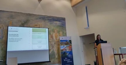 Prof. Dr. Nadine Spörer steht auf der Bühne und präsentiert die Unversitätsschule.