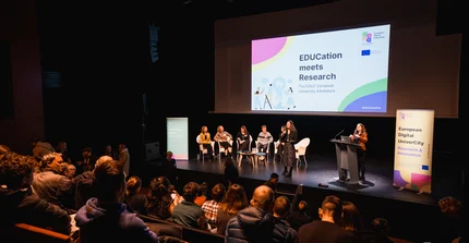 A stage with several speakers in front of a big audience.