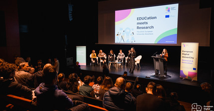A stage with several speakers in front of a big audience.