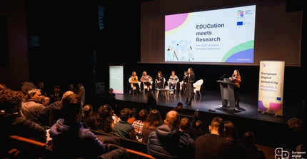 A stage with several speakers in front of a big audience.