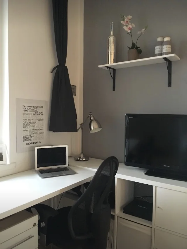Ein sehr aufgeräumter Schreibtisch in einer Zimmerecke. Daneben steht ein Fernseher