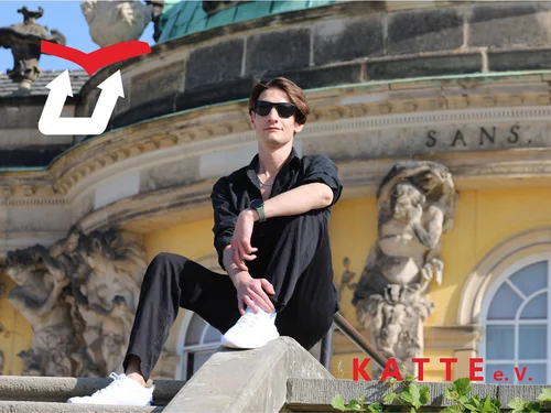 Eine Person mit Sonnebrille sitzt vor einem historischen Gebäude