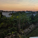 Sonnenuntergang auf Bali von einer erhöhten Position aus fotografiert. Eine Szene mit Palmen und Häusern.