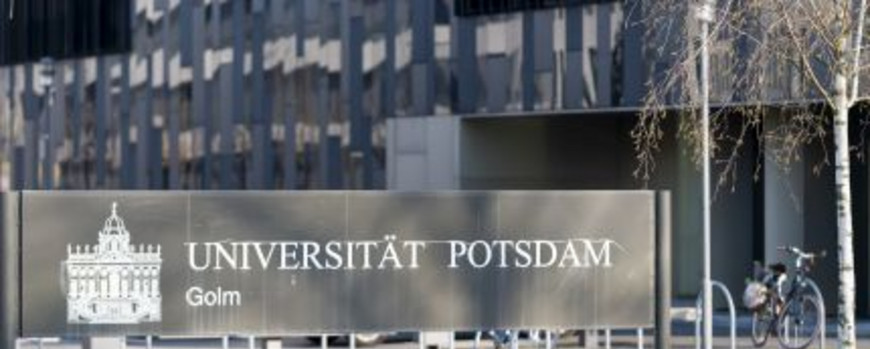 Schild mit Schriftzug „Universität Potsdam“ vor der Fassade eines schwarzen Gebäudes