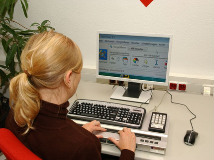 Eine Frau sitzt an einem Computer mit einer Seh-Hilfe.