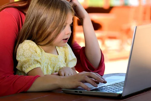 Eine Frau sitzt mit ihrem Kind auf dem Schoß vor einem Laptop.