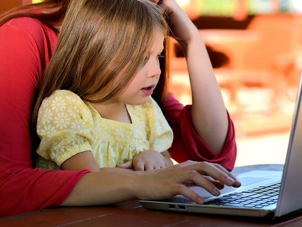 Eine Frau sitzt mit ihrem Kind auf dem Schoß vor einem Laptop.