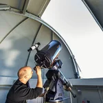 This image shows a scholar who is looking through a telescope in an observatory.