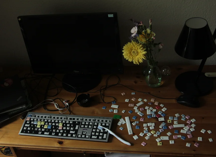 Auf einem Schreibtisch liegt eine Tastatur, die Tasten sind teilweise ausgebaut und liegen daneben. Auf der Tastatur liegt eine Zahnbürste