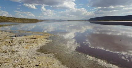 Wolken, die sich im Magadi-See in Kenia spiegeln, der sich im östlichen Zweig des ostafrikanischen Grabensystems befindet. Im Hintergrund die hoch aufragenden Flanken der Grenzverwerfungen des Grabens.