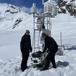 Field site Dresdner Hütte: Two scientists with a mobile CRNS sensor on a sled standing next to measuring devices installed at a alpine hillslope | Photo: Cosmic Sense Consortium