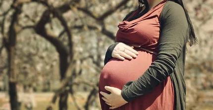 Eine hochschwangere Frau, die ihre Hände auf den Bauch gelegt hat.