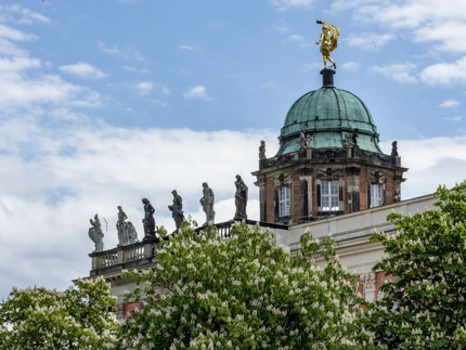 Roof of the historic north commun with figures on the edge and on the dome, on the lower edge blooming chestnut trees