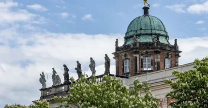 Dach des historischen Nordcommuns mit Figuren am Rand und auf der Kuppel, am unteren Rand blühende Kastanienbäume