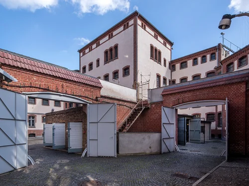 Innenhof mit hellen Gebäuden und roten Ziegelmauern und Eisentoren