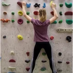 Junge Frau in Sportkleidung klettert an Kletterwand mit sehr vielen bunten Griffen