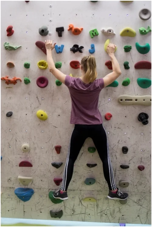 Junge Frau in Sportkleidung klettert an Kletterwand mit sehr vielen bunten Griffen