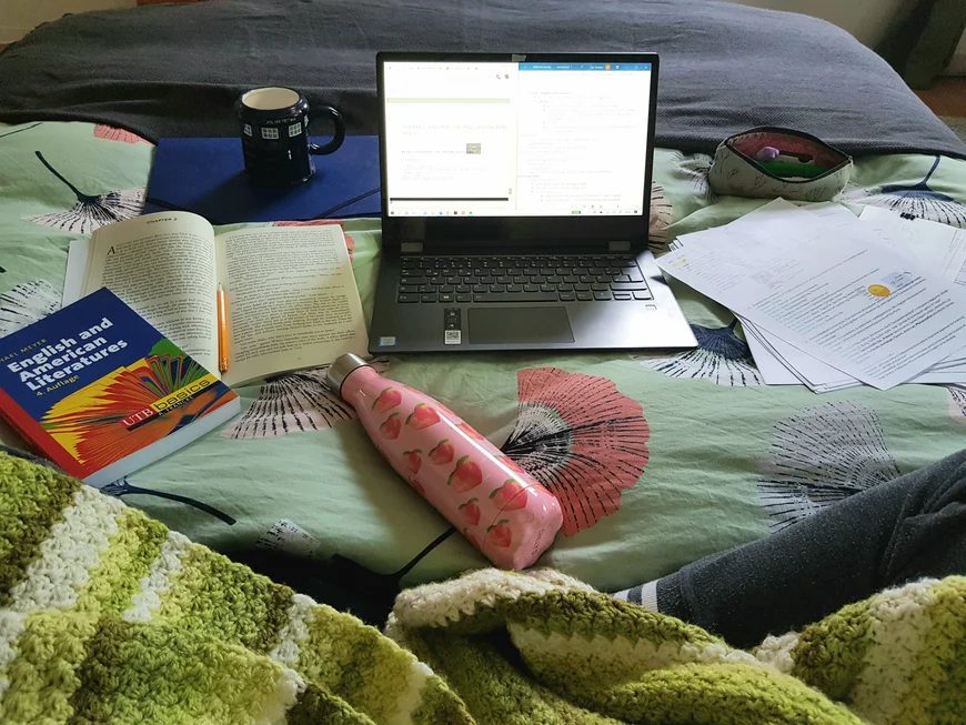 Laptop, Bücher und Schreibsachen auf einem Bett