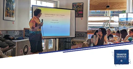 Vortragender neben Leinwand in einem Café mit interessierten Zuhörern