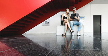 Zwei Personen sitzen unter einem roten Treppenaufgang.