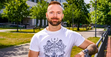 Halbporträt von Dr. Alex Miklashevsky mit Bart und kurzen Haaren, weißes T-Shirt mit Aufdruck im Park