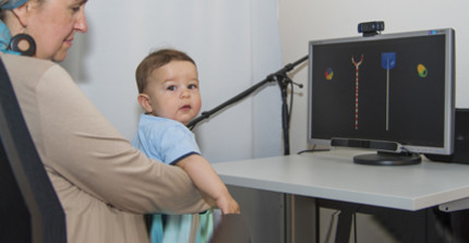 Kind sitzt auf Schoß der Mutter und blickt auf einen Bildschirm