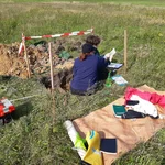Zwei Personen auf Wiese in gegrabener Grube