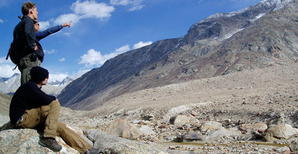 Drei Wissenschaftler stehen in steinigem Gebirge und deuten auf einen Felsen