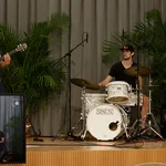 Eine dreiköpfige Band (Schlagzeug, Bass, Gitarre) spielt auf einer kleinen Bühne.