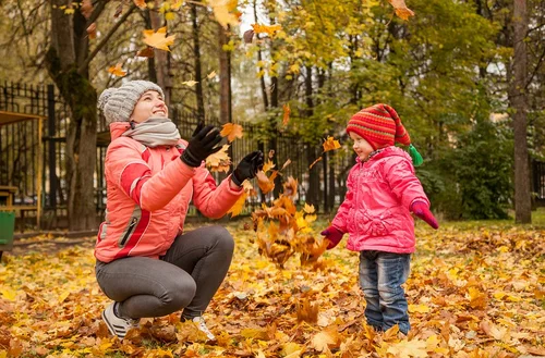 Eine Frau und ein Kind spielen im Herbstlaub. Die Frau wirft Laub nach oben.