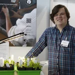 Mann neben tragbaren Gewächshaus an einem Messestand, lächelnd in die Kamera