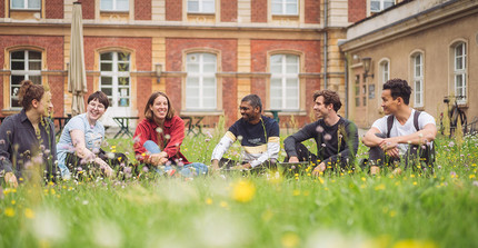 Studierende auf einer Wiese sitzend vor historischen Gebäuden der Uni Potsdam.