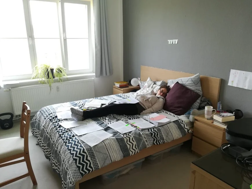 Ein Studentin liegt auf ihrem Bett und döst, um sie herum sine Unterlagen und Ordner verteilt