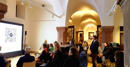 Eine veranstaltung im Brandenburg Museum. Mehrere Menschen sitzen oder stehen und betrachten einen Bildschirm im Ausstellungsbereich des Bbg. Museum.