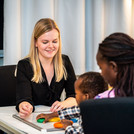 This image shows an examination in the BabyLab. We see a researcher and a mother with her child.