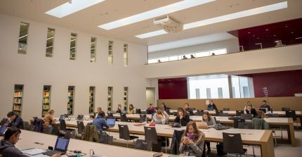 Students sit at workstations in a large reading room at the university library