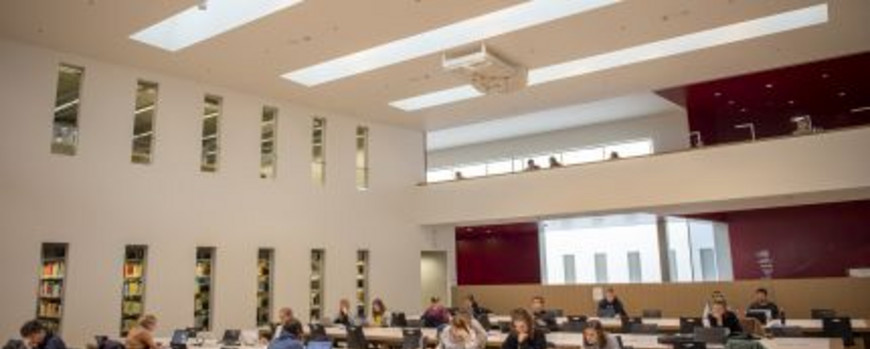 Studierende sitzen an den Arbeitsplätzen in einem großen Lesesaal der Universitätsbibliothek