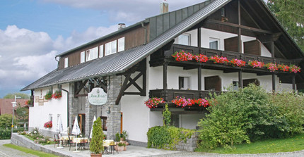 Ein weißes Haus, mit schwarzem Dach und roten Blumen in Balkonkästen