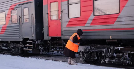 Anschnitt eines rot/grauen Zuges im Schnee, davor ein Mensch, der an den Rädern des Zuges arbeitet.