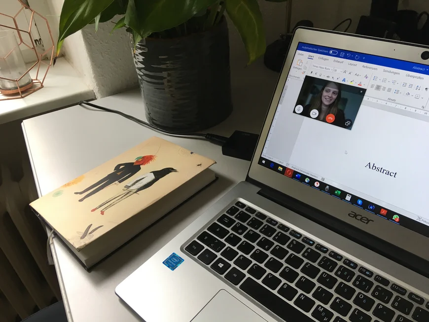 Ein Laptop, danaben liegt ein dicker Terminplaner. Auf dem Bildschirm ist Word geöffnet und darüber ein Fenster eines Videochatprogramms, zu sehen ist das Gesicht einer jungen Frau