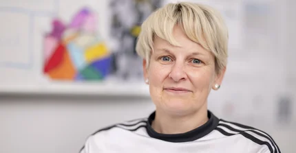 Porträtfoto von Dr. Bettina Buchholz im weißen T-Shirt mit blonden kurzen Haaren, im Hintergrund unscharf fotografierte Kunst