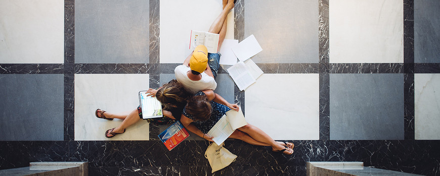 Drei Studierende sitzen mit Büchern und Notizen auf dem Boden.