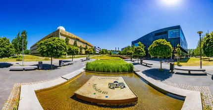 Aufnahme von zwei Gebäuden, in der Mitte ein Wasserspiel