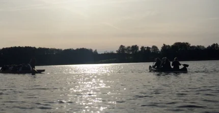 2 Kanus fahren auf einem See vor untergehender Sonne
