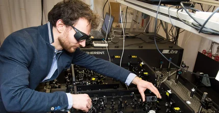 Eine Person justiert einen Versuchsaufbau für ein optisches Experiment. Die Person trägt eine Laserschutzbrille.