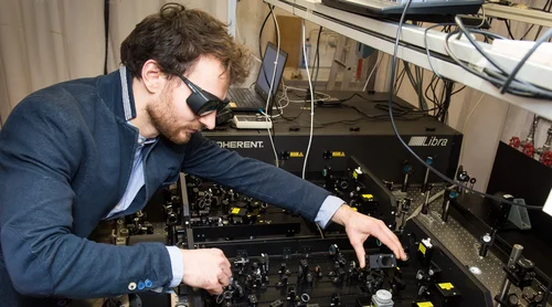 Eine Person justiert einen Versuchsaufbau für ein optisches Experiment. Die Person trägt eine Laserschutzbrille.