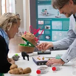 Eine Frau steht an einem Tisch mit Exponaten, ein Wissenschaftler erklärt.