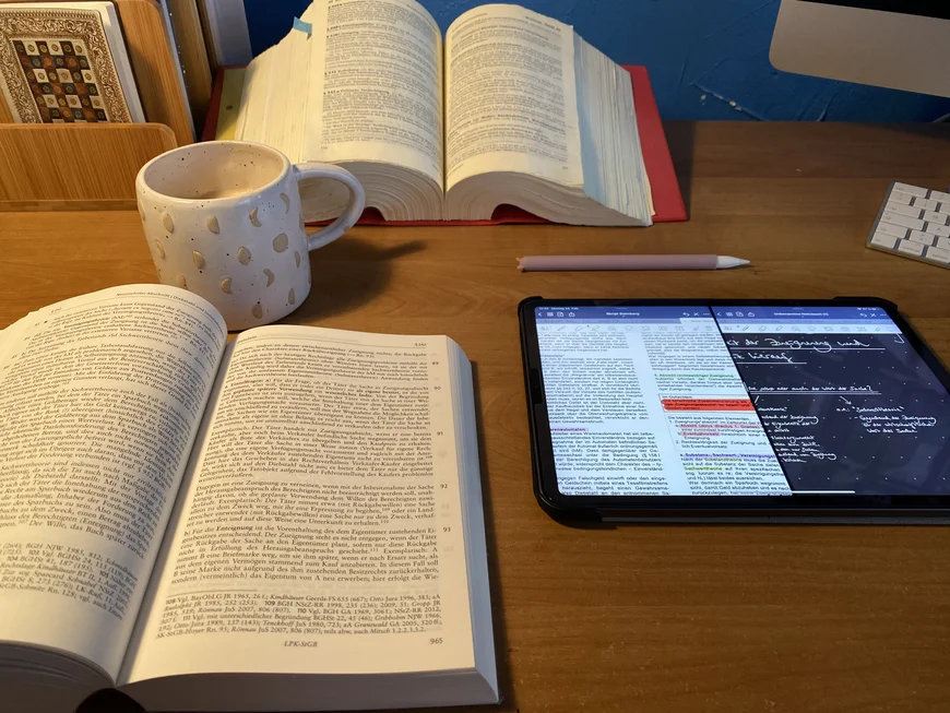 Stilleben aus aufgeschlagenen buch, daneben ein Tablet mit Tafelbild und Text, eine Tasse und ein weiteres Buch